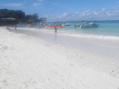 Wit zandstrand met turquoise zee en bootjes voor de kust, Kalimantan, Sulawesi & Molukken rondreis.