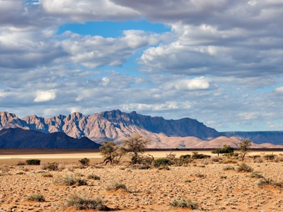 Woestijnlandschap bij Windhoek met rotsige bergen en acaciabomen onder een bewolkte lucht.