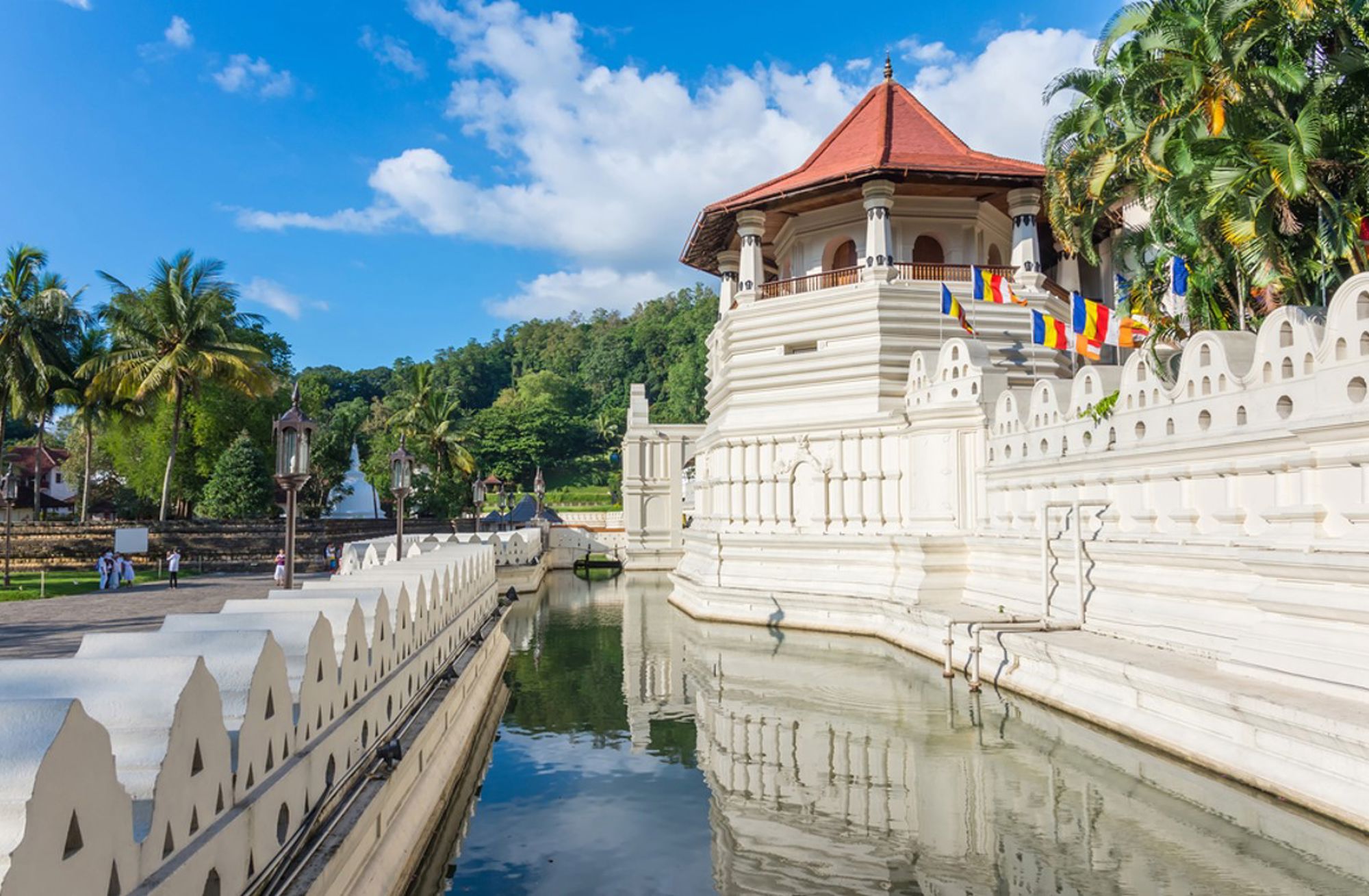 Tempel van de Tand in Kandy met witte muur, vlaggen en watergracht onder een blauwe lucht.