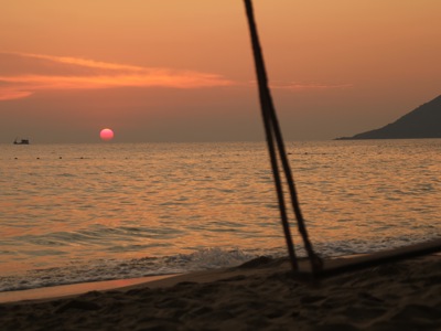 Zonsondergang boven zee vanaf het strand in Thailand, met silhouet van een eiland in de verte.