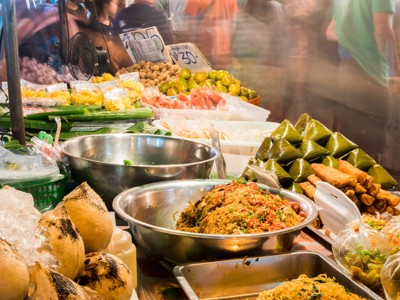 Streetfoodkraam op een avondmarkt in Thailand met noedels, loempia’s, fruit en kokosnoten.