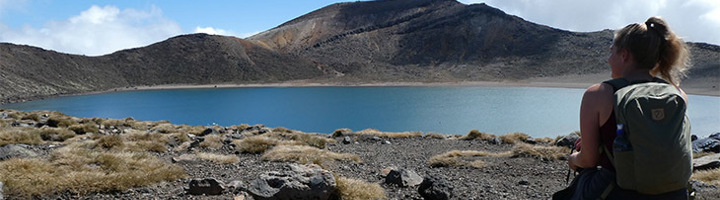 Wandelaar met rugzak bij een helderblauw kratermeer op de Tongariro Alpine Crossing in Nieuw-Zeeland.