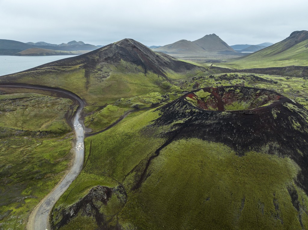 Groene vulkaankrater en lavavelden in IJsland langs een kronkelende weg.