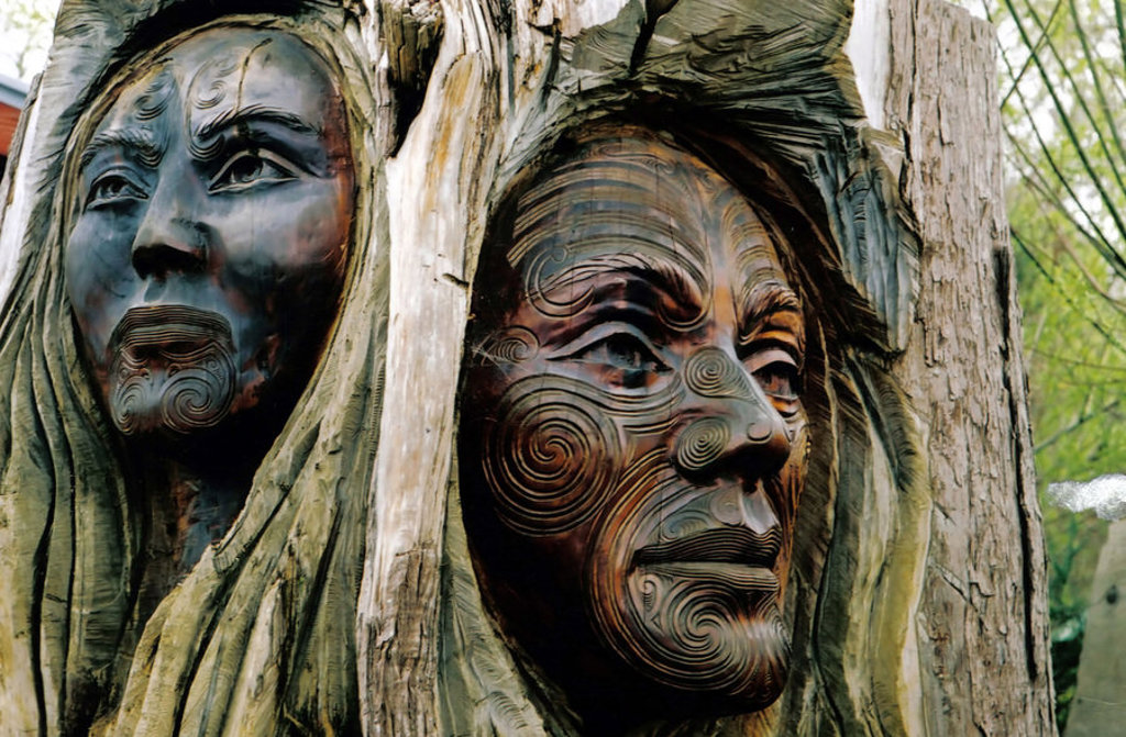 Houtsnijwerk met Māori-gezichten en traditionele patronen tijdens een groepsrondreis Nieuw-Zeeland.