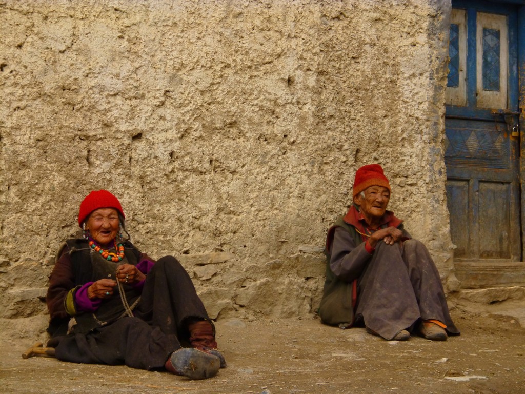 Twee oudere bewoners met rode mutsen zitten tegen een muur in Ladakh, India.