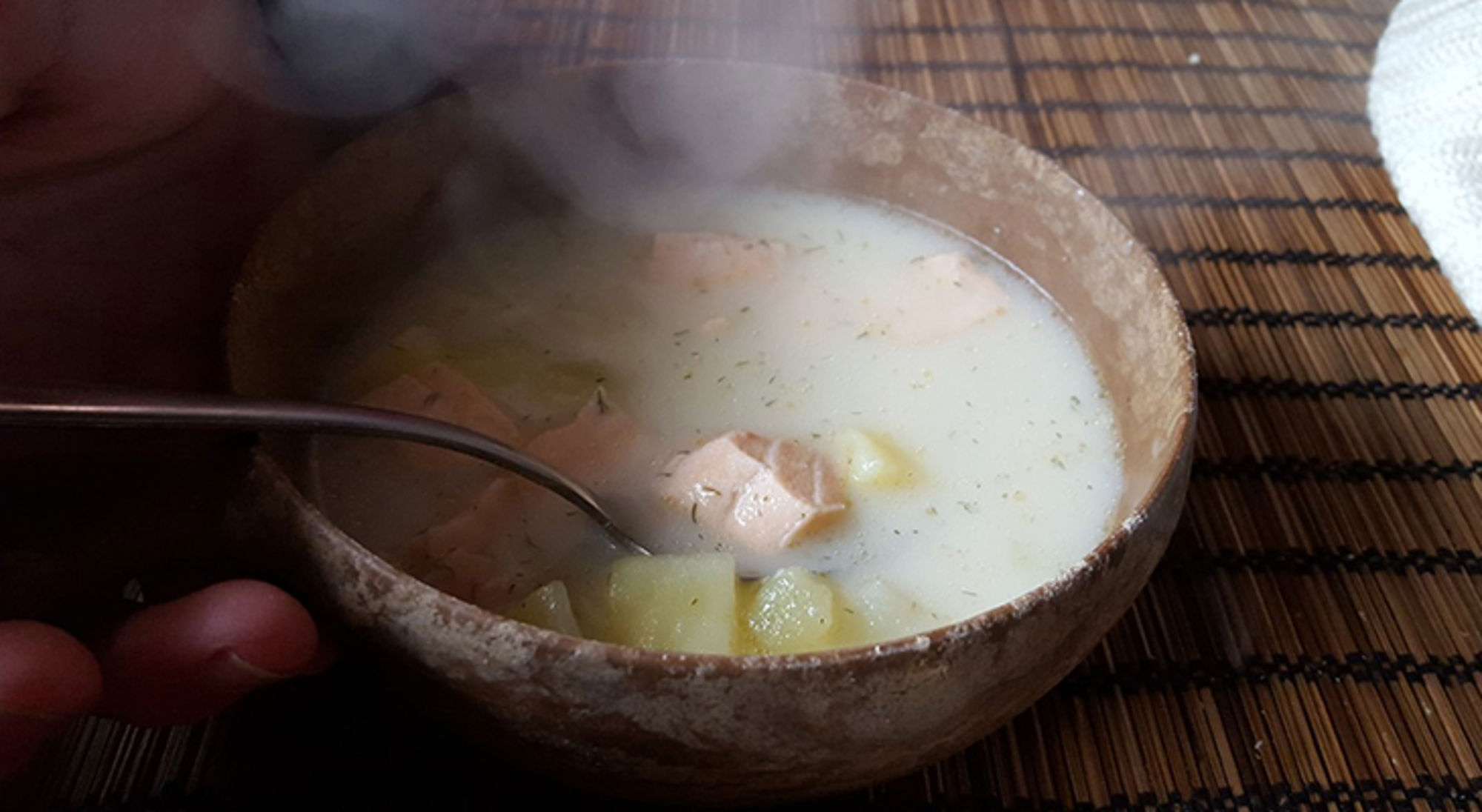 Kom dampende kokossoep met tofu en aardappelblokjes op een bamboemat.