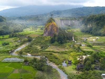 Groene rijstvelden en rivier in de Harau-vallei op Sumatra, met steile rotswand en heuvels.