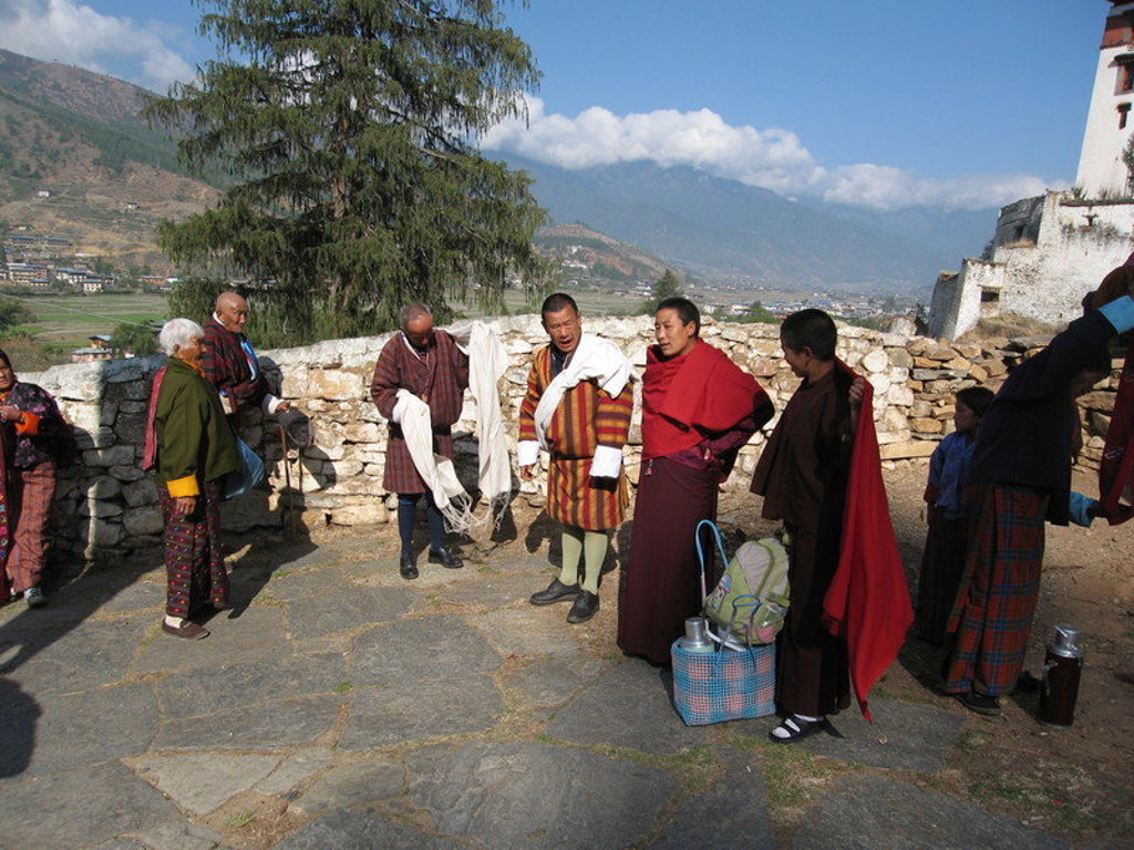 Monniken en locals op binnenplaats van klooster in Bhutan, met Himalaya-bergen op de achtergrond.