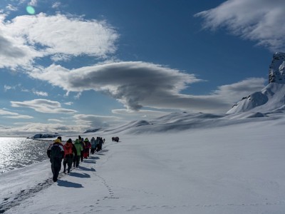 Groep wandelt over een besneeuwde kustlijn op Spitsbergen tijdens de 12-daagse route, met bergen en zee op de achtergrond.