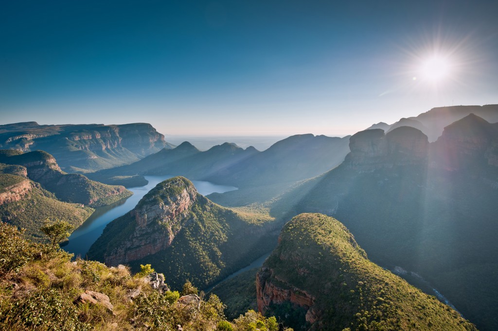 Panoramisch uitzicht op de Blyde River Canyon in Zuid-Afrika met rivier, rotsformaties en zon boven de bergen.