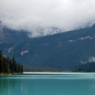Turquoise bergmeer in West-Canada met dennenbos, mistige bergen en kanoërs op het water.