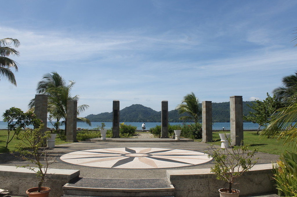 Uitzicht op zee en groene heuvels vanaf een promenade met palmbomen op de Molukken, Indonesië.