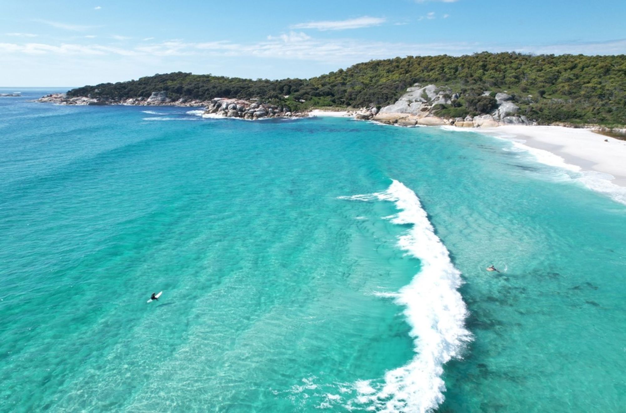 Turquoise zee met brekende golven bij een wit zandstrand en rotsachtige kust in Australië.