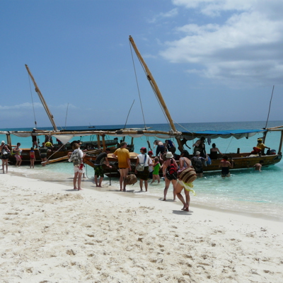 Bezoekers stappen vanaf het strand in een dhow voor de Safari Blue-bootexcursie op turquoise zee bij Zanzibar.