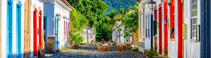 Kleurrijke straat met kinderkopjes en historische huizen in Paraty, Brazilië, met groene bergen op de achtergrond.