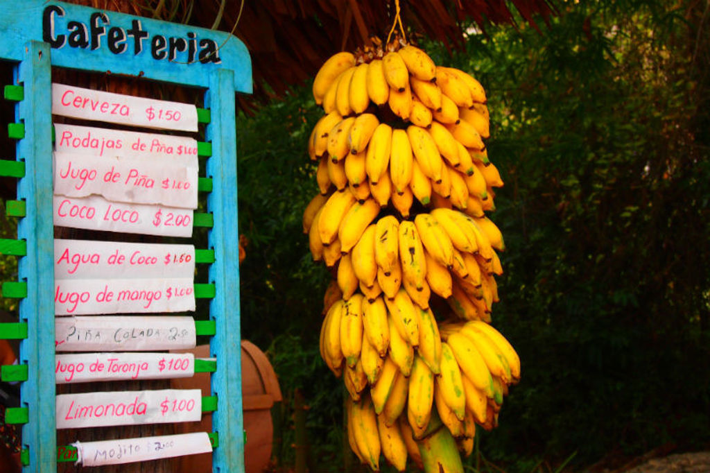 Menubord van een cafetaria naast een grote tros bananen tijdens een groepsrondreis in Cuba.