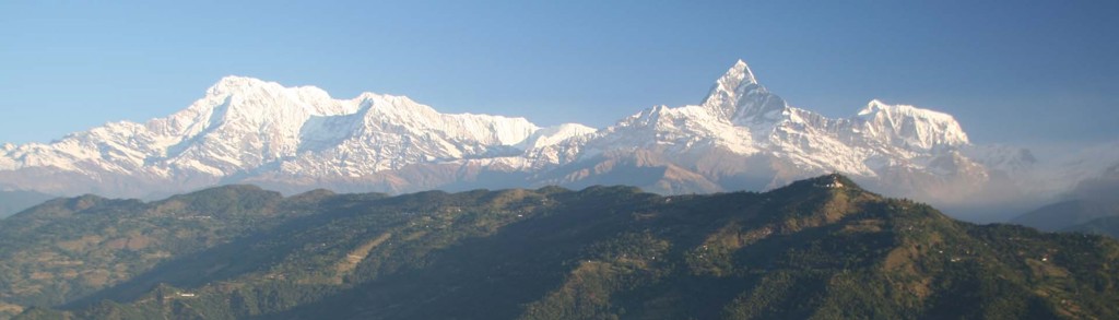 Panorama van de besneeuwde Himalaya in Nepal, met bergtoppen boven groene heuvels.