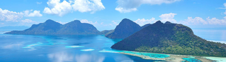 Panoramisch uitzicht op tropische eilanden met turquoise lagune en koraalrif onder een blauwe lucht.