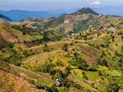 Groene heuvels met akkers en een dorpje langs een slingerende weg in Myanmar.