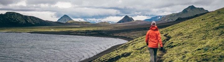 Wandelaar op de Laugavegur Trail langs een meer, met groene heuvels en bergen in IJsland.