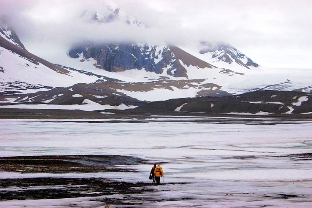 Wandelaars in poolkleding op het ijs bij besneeuwde bergen op Spitsbergen tijdens een groepsrondreis.