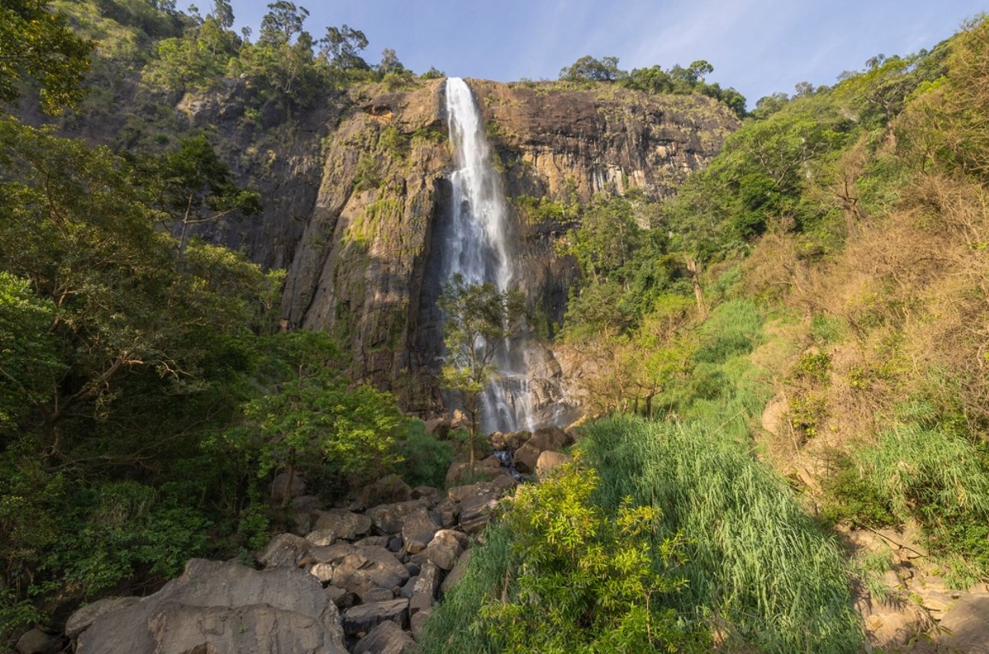 Hoge waterval die langs een rotswand naar beneden stort, omringd door groen in Sri Lanka.