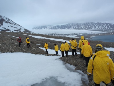 Wandelaars in gele jassen trekken over sneeuw en rotsen langs een fjord in de Noordpool.