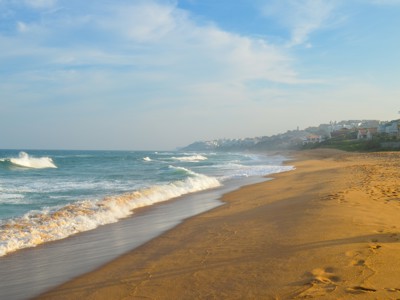 Zandstrand aan de Zuid-Afrikaanse kust met golven en huizen op de achtergrond, Route Zuid-Afrika.