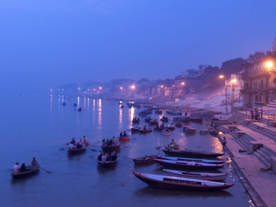 Avondbeeld van de Ganges in Varanasi met boten en verlichte ghats langs de rivier.