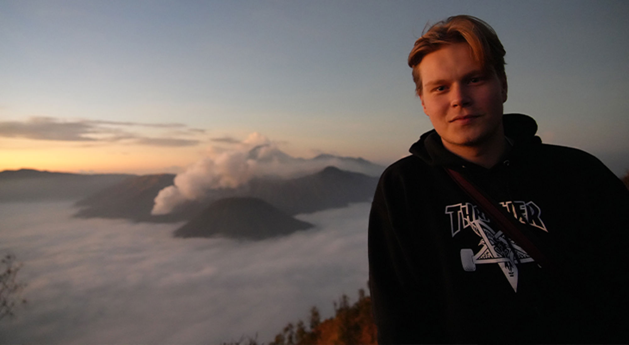 Olivier in Indonesië Jonge man op uitkijkpunt bij zonsopkomst met mistige bergen op de achtergrond.