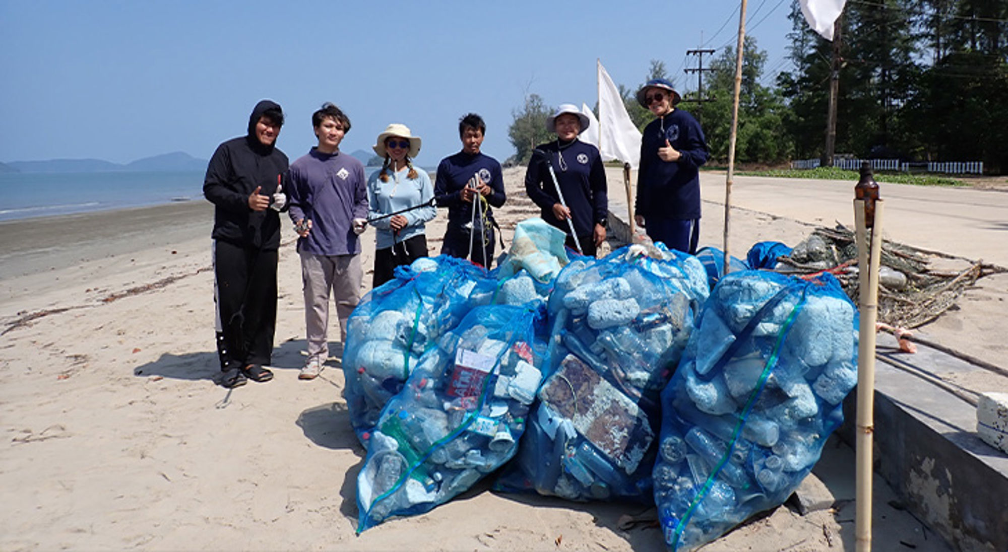 Vrijwilligers poseren op het strand met grote zakken verzameld plastic afval na een beach clean-up.