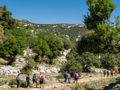 Wandelaars met rugzakken op een bergpad door rotsachtig groen landschap op Sardinië, dag 5 van de 8-daagse wandelvakantie.