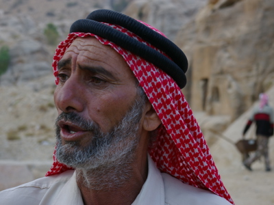 Portret van een man met rood-wit keffiyeh in de rotsstad Petra, Jordanië.