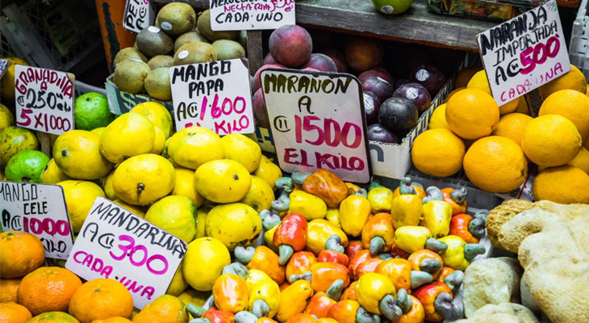 Producten/lokale specerijen San Jose Kleurrijke fruitkraam op een markt in Costa Rica met mango’s, mandarijnen, cashewnoten en prijsbordjes.