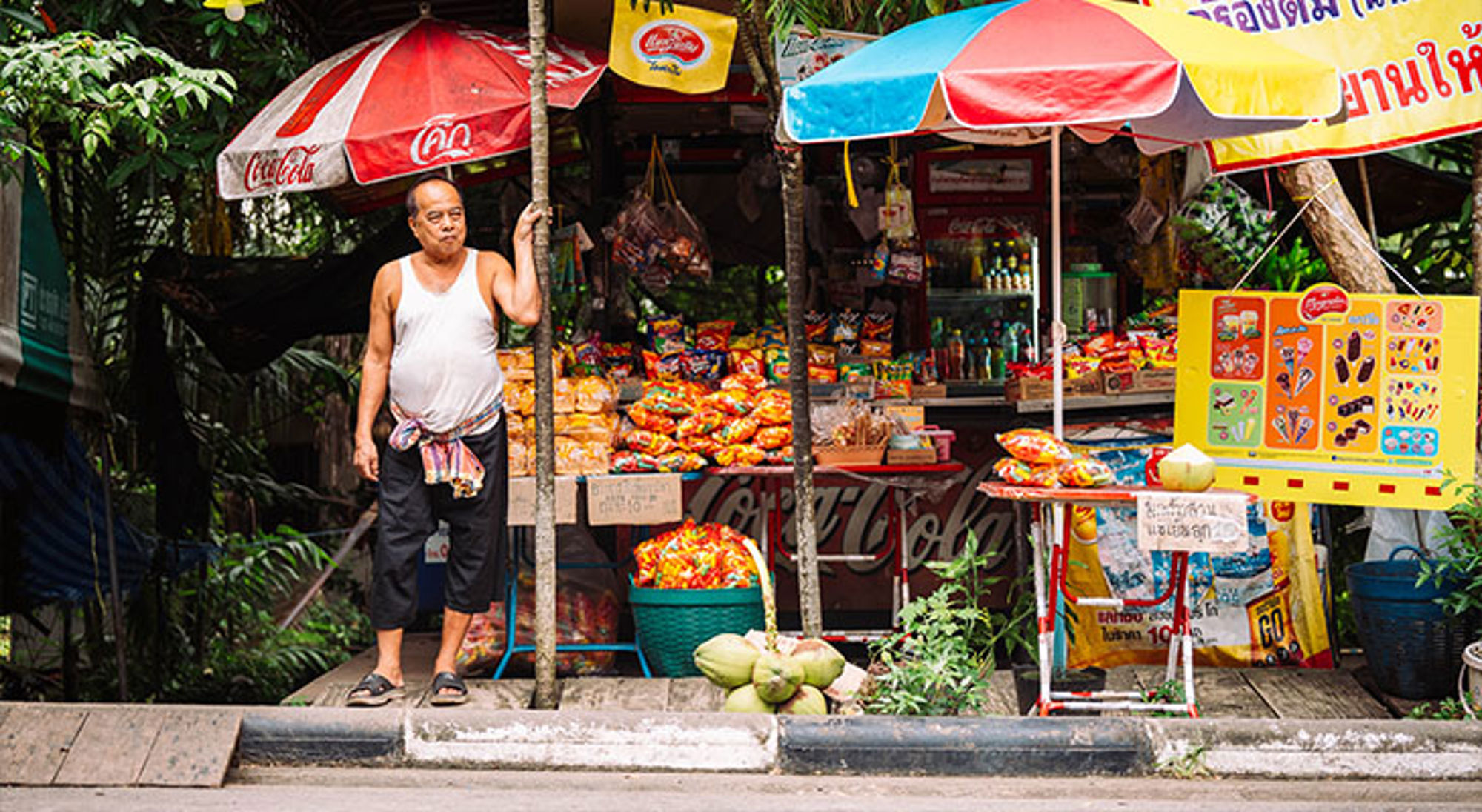 Thaise bevolking Straatkraam met snacks en drankjes onder kleurrijke parasols, met verkoper ervoor.