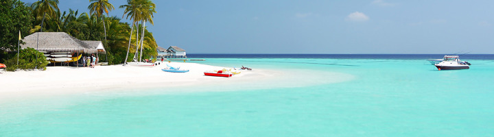Wit zandstrand op de Malediven met palmbomen, helderblauwe lagune en bootjes.