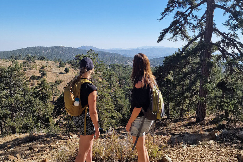 Wandelaars met rugzak kijken uit over berglandschap en dennenbos tijdens wandelvakantie op Cyprus.