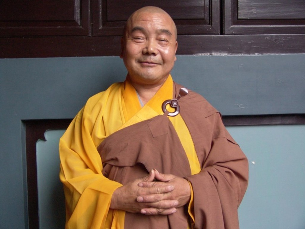 Monnik in geel en bruin gewaad poseert bij een tempelmuur tijdens familiereis Myanmar.