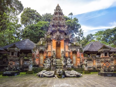 Balinese tempelpoort met beeldhouwwerk en stenen beelden, omringd door tropisch groen op Bali.