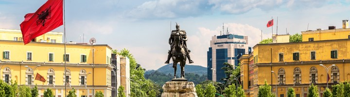 Standbeeld van Skanderbeg op het Skanderbegplein in Tirana, Albanië, met Albanese vlaggen en kleurrijke gebouwen.