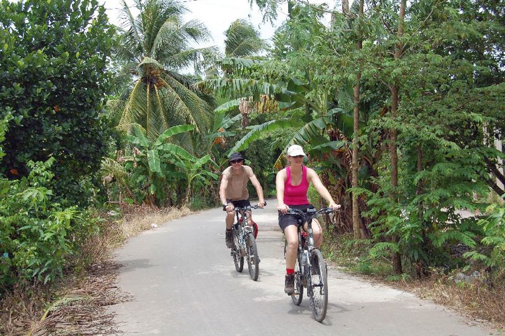 Fietstocht tijdens groepsrondreis Vietnam langs een landelijke weg met palmen en bananenbomen.