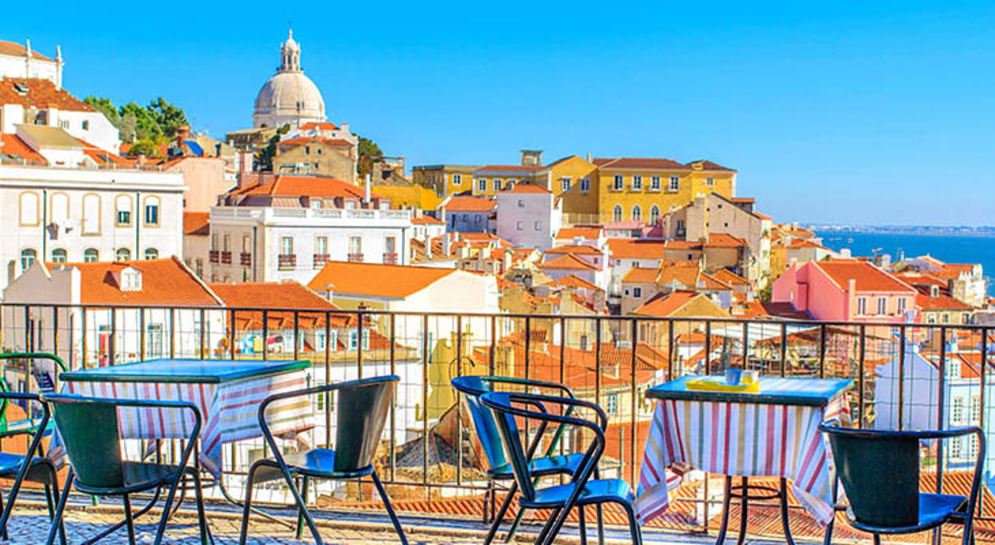 Terras met tafels en stoelen met uitzicht op kleurrijke daken en de koepel van het Nationaal Pantheon in Lissabon.