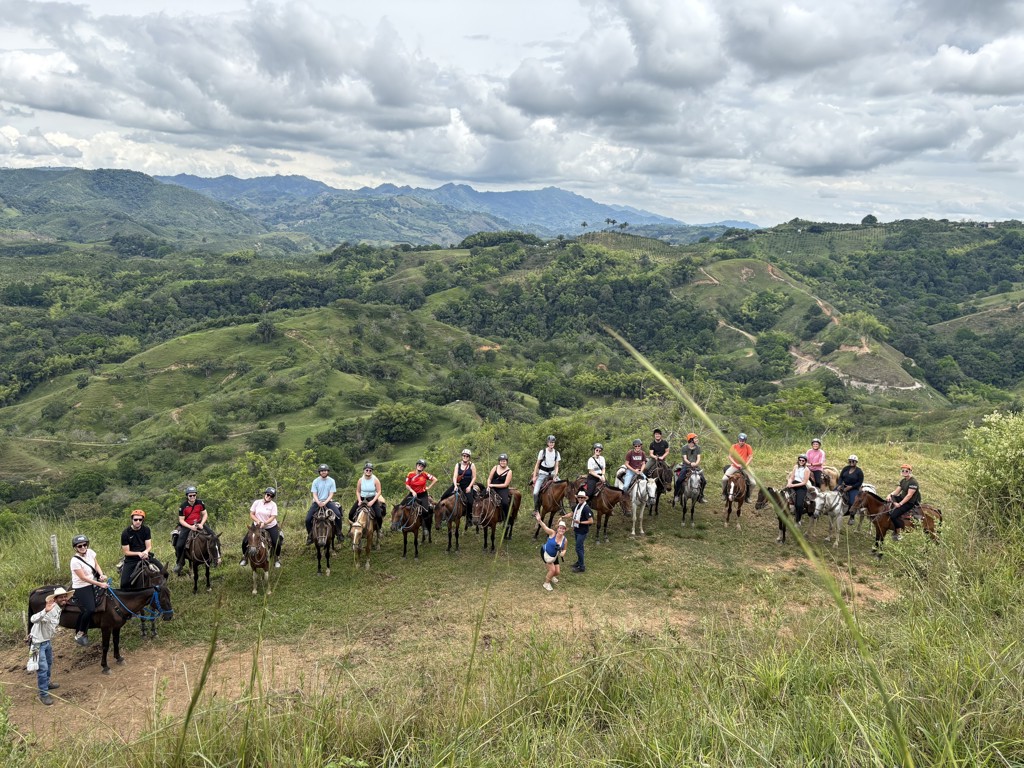 Groep 22-35ers te paard met gids in de groene heuvels van Colombia tijdens een rondreis.