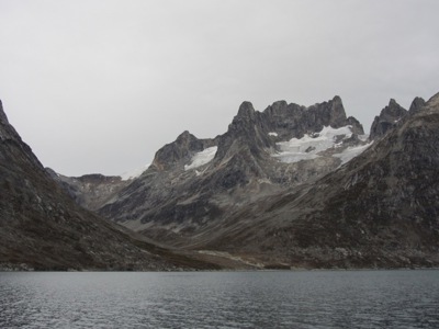 Berglandschap in Groenland met steile rotsen, sneeuwvelden en een fjord op de voorgrond.