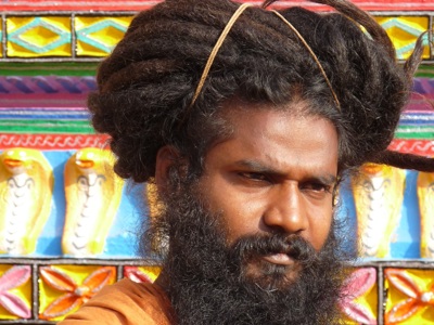 Portret van een hindoe sadhu met grote haarknot en lange baard voor een kleurrijke tempelmuur in Orissa.