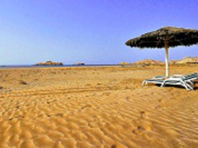 Zandstrand in Oman met rieten parasol en ligbedden aan zee.