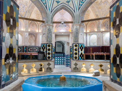 Interieur van een traditionele Iraanse hammam met kleurrijke tegels, bogen en een klein waterbassin.