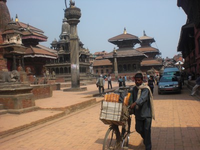 Straatbeeld op Patan Durbar Square in Nepal met tempels en een fietskar met handelswaar.