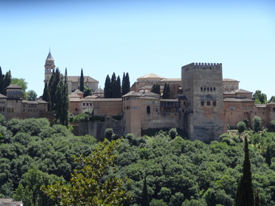 Alhambra in Granada, Andalusië, met paleismuren en torens boven groen landschap.