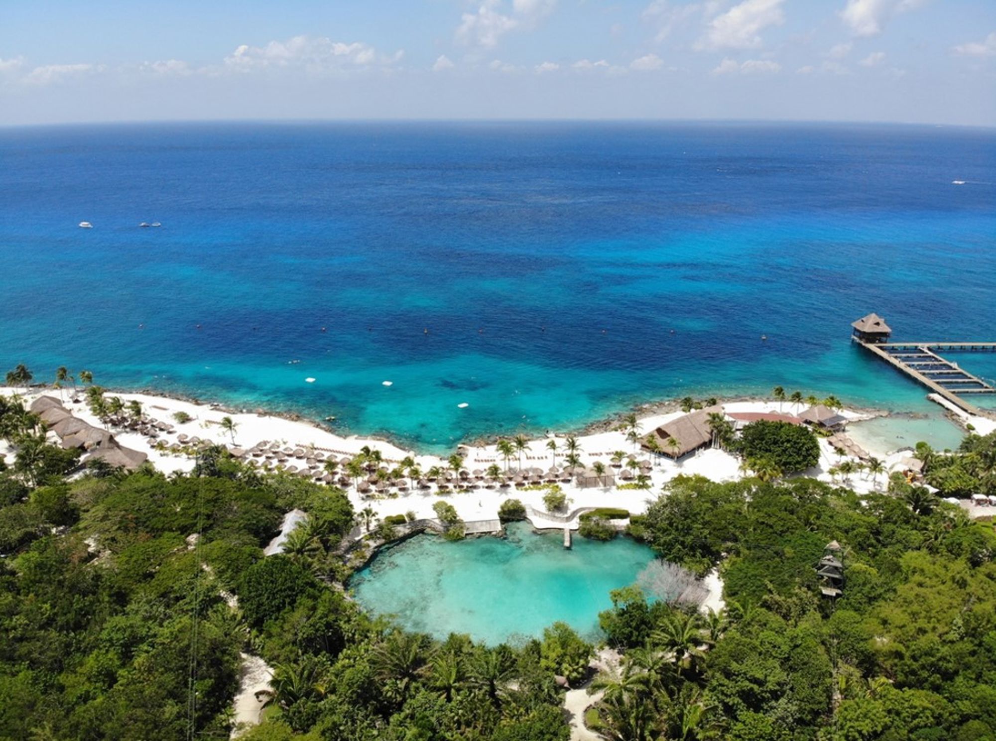 een wit zandstrand met palmbomen en helderblauwe zee aan de kust van Mexico.